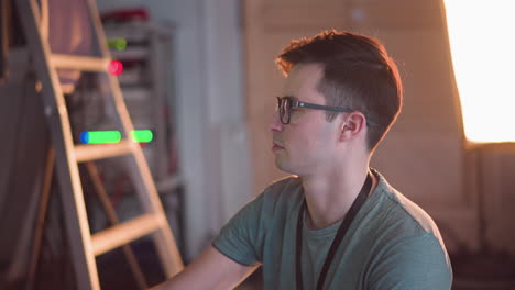 person adjusting video equipment in tv studio, focused on monitor and control panel. studio lights and equipment visible in background while working on broadcast setup and settings