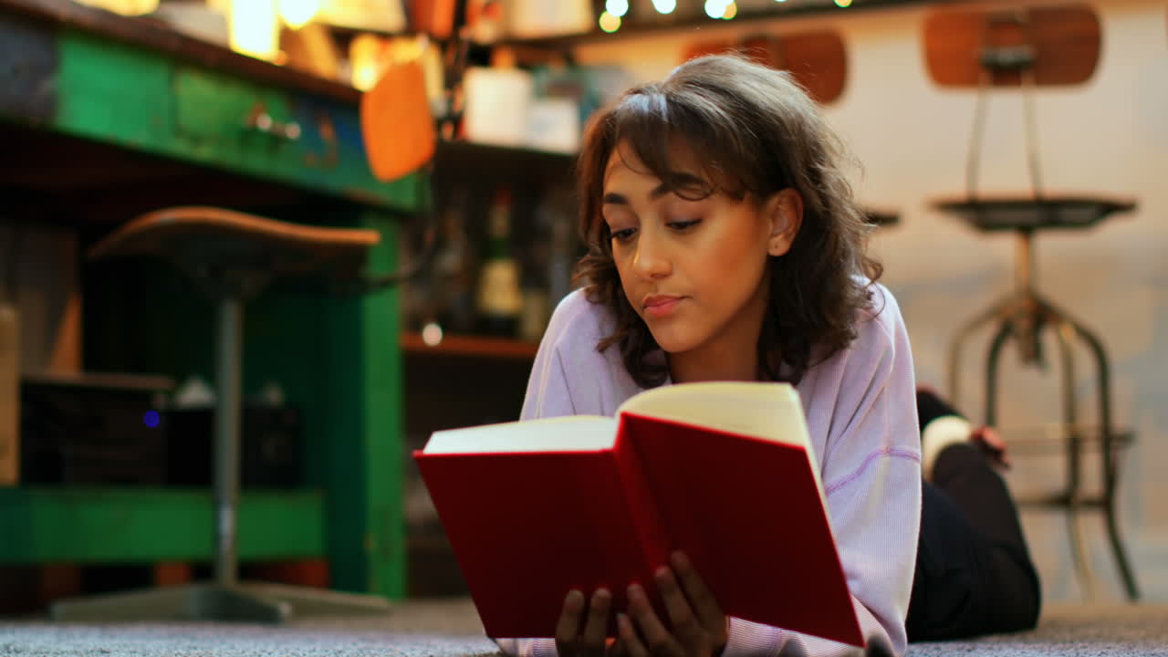 escena escolar con una chica tendida en el suelo leyendo un libro rojo