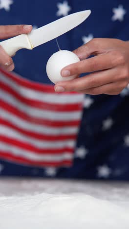 preparing an egg with a knife on an american flag apron