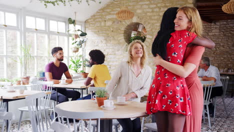 Three-young-adult-female-friends-hugging-each-other-on-arriving-at-a-restaurant,-over-shoulder-view