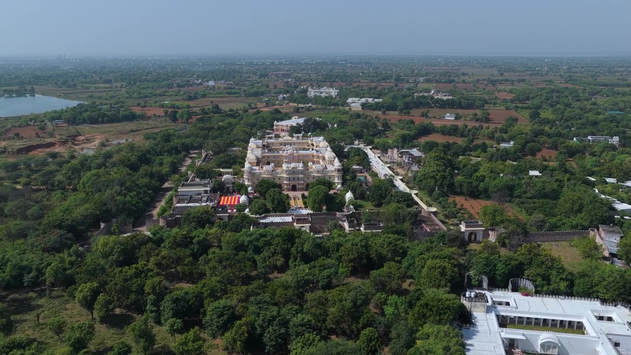 Un'ampia ripresa aerea cinematografica di un hotel palazzo storico bianco circondato da lussureggianti foreste verdi e paesaggi rurali in India.