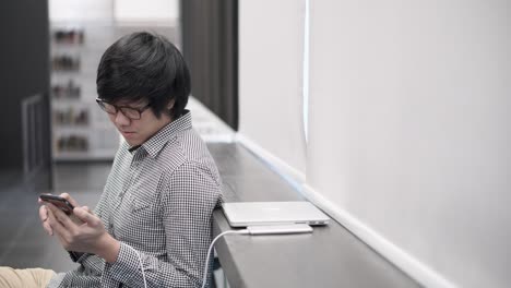 소셜미디어 애플리케이션을 사용하면서 기기를 충전하는 젊은 아시아 사업가: 작업 공간 개념에서 도시 라이프 스타일