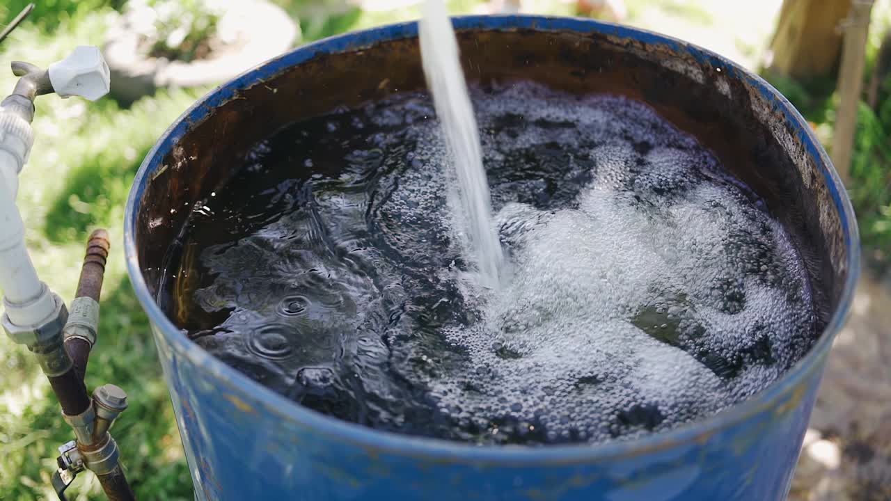 인필드의 에서 물이 파란 금속 배럴에 흘러 들어가서 그것을 채운다.