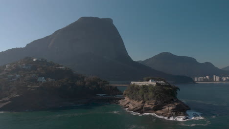 rotational aerial pan showing the joatinga beach on a hazy backlit day with the gavea mountain behind revealing the wider well known cityscape of rio de janeiro in the background