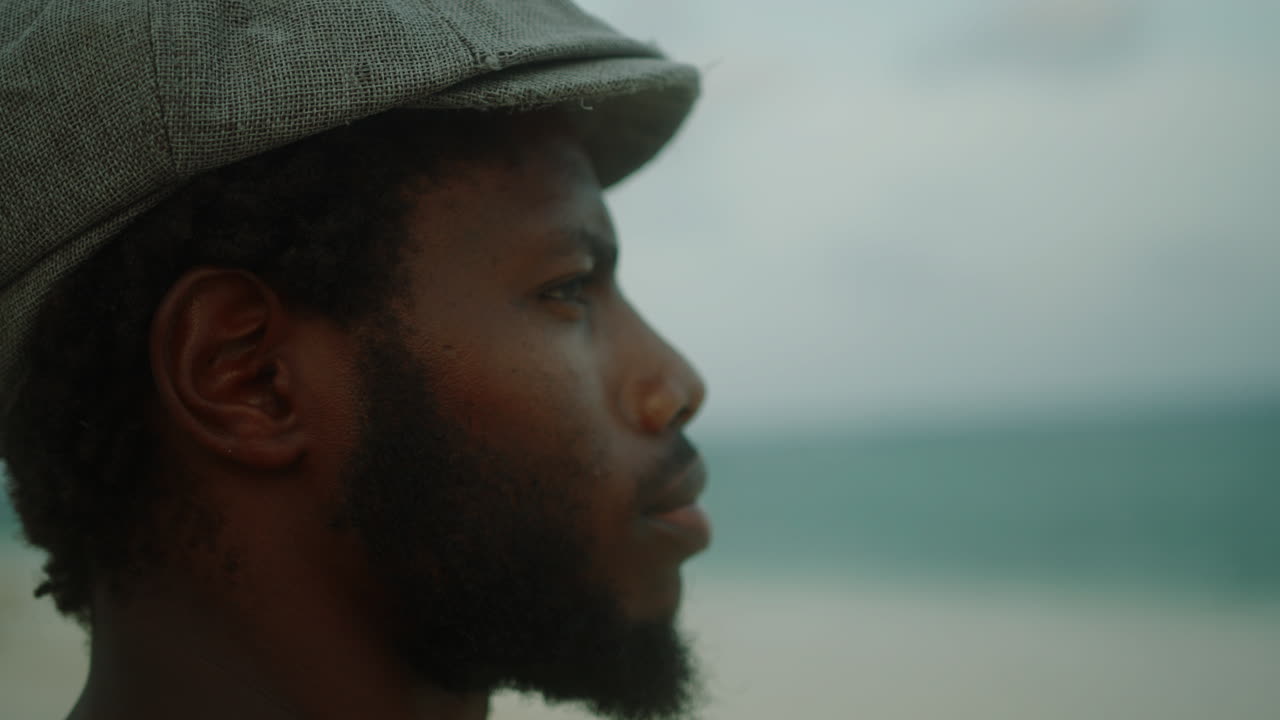 Close-up of handsome, bearded young black man looks introspectively out to sea