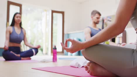 instructora caucásica, hombre y mujer diversos sentados en posición de loto en esteras en la clase de yoga