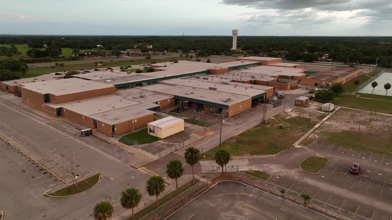 Closed American school in Brandon, Florida at sunset time. Aerial approaching shot. Rooftop of campus building in suburb of town.