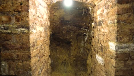hand held shot inside old bricked underground wine cellar, illuminated wall hole