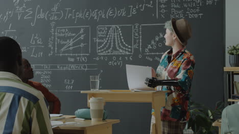 a person with a prosthetic arm presents scientific information on a blackboard in a lecture setting