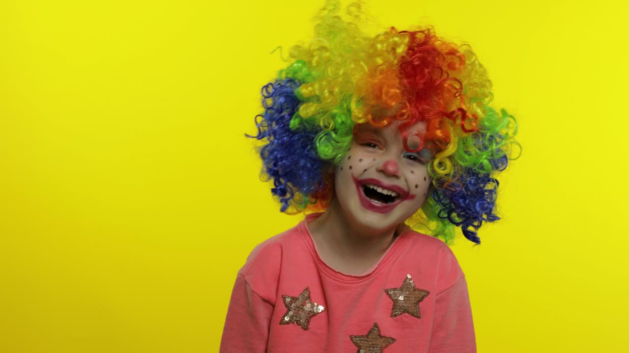 una niña payasa con una peluca arco iris haciendo caras tontas. divirtiéndose, sonriendo, riendo. halloween