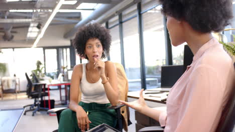 biracial woman in business casual attire discussing with colleague in office