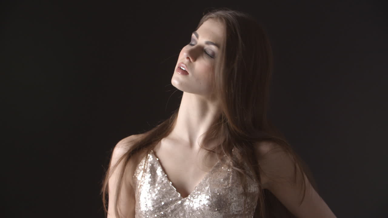 저녁 옷을 입은 젊은 여성이 머리를 던지고 머리를 흔들고 있습니다.