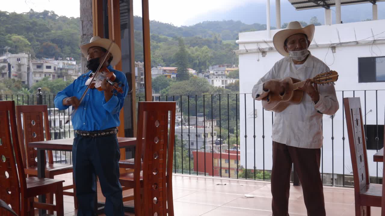Two musicians playing violin and guitar on a balcony overlooking a mountainous village