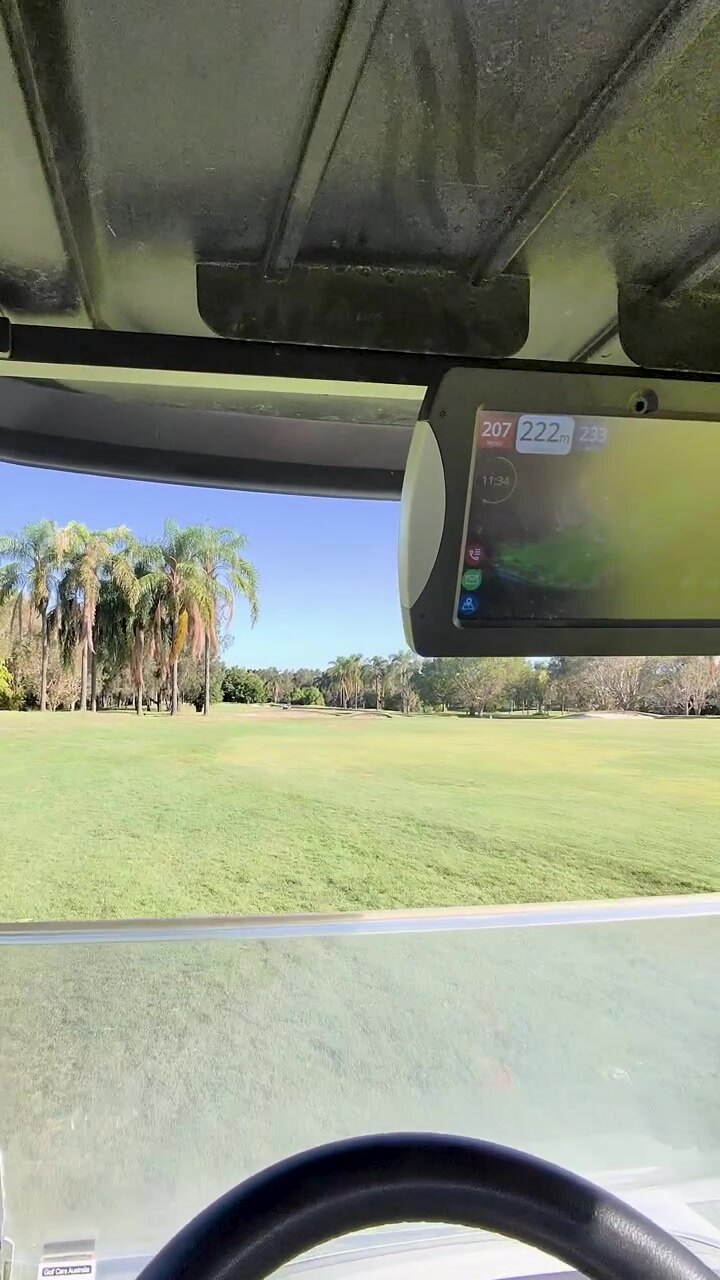 Point-of-view golf cart ride across sunny green fairway with palm trees and dashboard screen