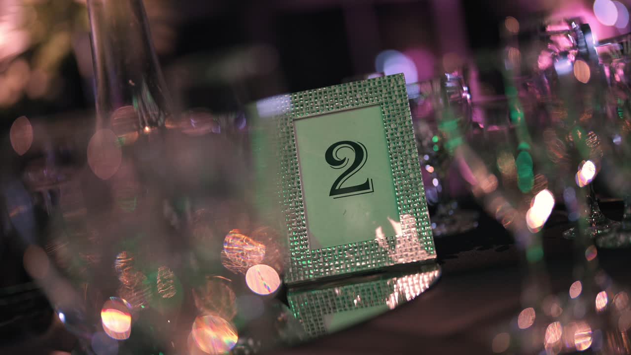 Elegante segnatavolo numero 2 su una superficie a specchio in occasione di un evento di lusso esclusivo, con luci bokeh scintillanti che creano un effetto sfocato sullo sfondo raffinato della festa