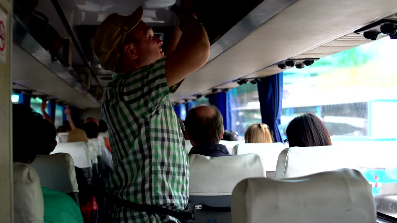 A man walks through the cabin of the bus, removes the bag on the luggage rack and sits down