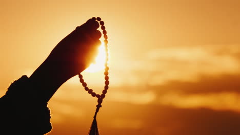 hand holds rosary against the sky and the setting sun sincere prayer and meditation