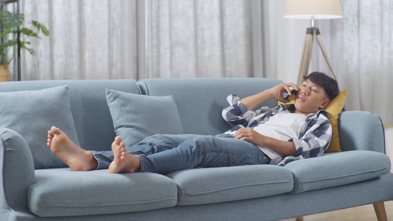 집 의 거실 의 소파 에 누워 있는 동안 스마트폰 으로 대화 하는 아시아 청소년 소년 의 몸 이 가득 차 있다