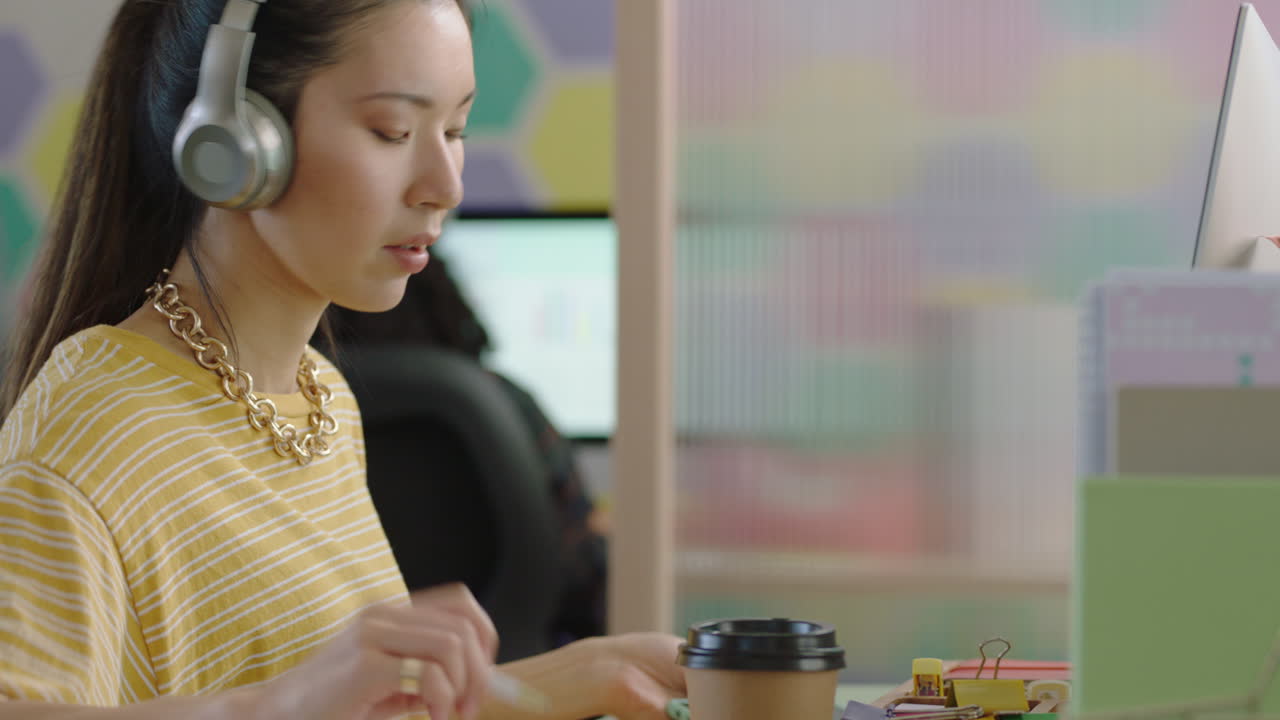 da vicino bellissima giovane studentessa asiatica che usa il computer brainstorming che lavora a un progetto creativo che si gode lo studio in un ufficio moderno colorato che ascolta musica indossando le cuffie