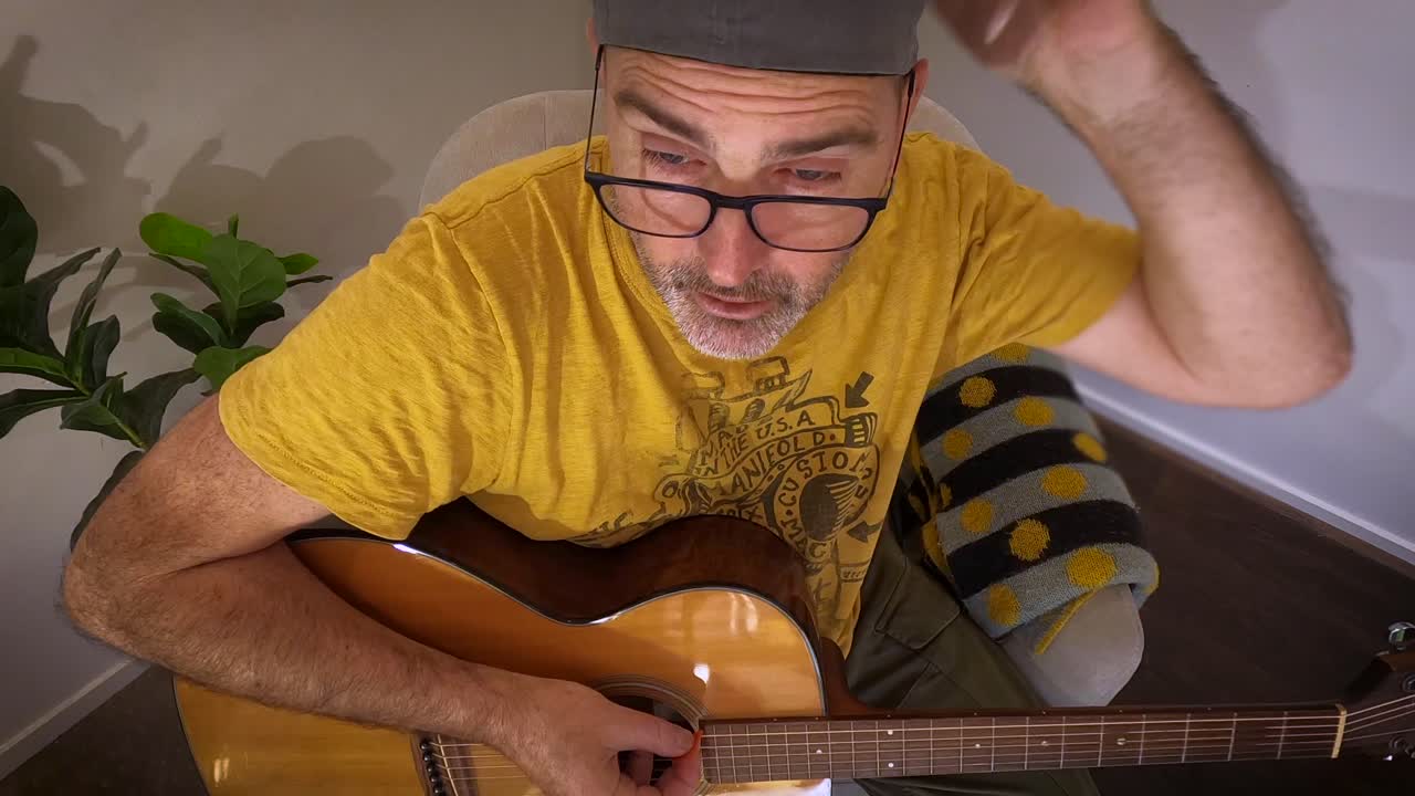 un anciano cansado en un pequeño escenario de esquina afina una guitarra y habla con la audiencia