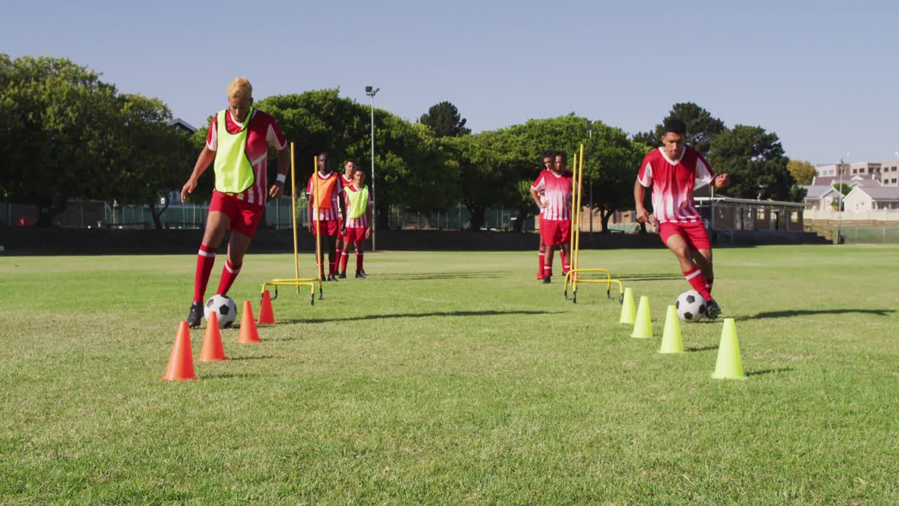 Video of diverse group of male football players warming up on field,running and kicking ball