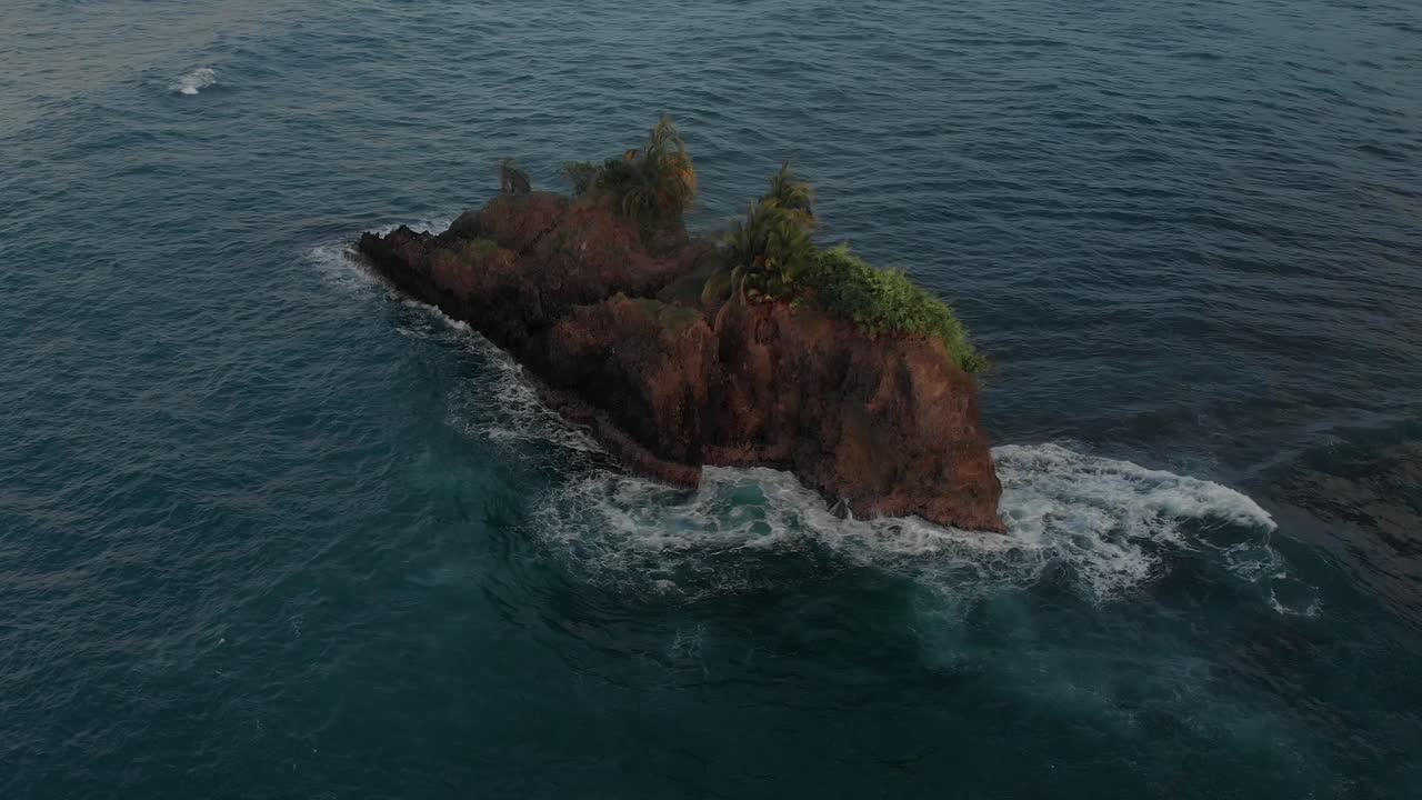 Sea waves crashing and splashing on a rock island in Costa Rica - aerial