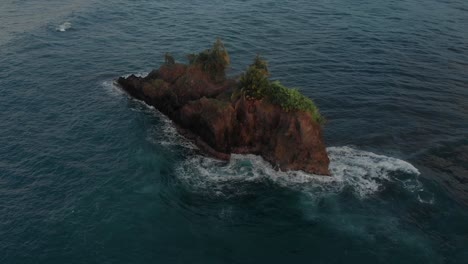 sea waves crashing and splashing on a rock island in costa rica - aerial