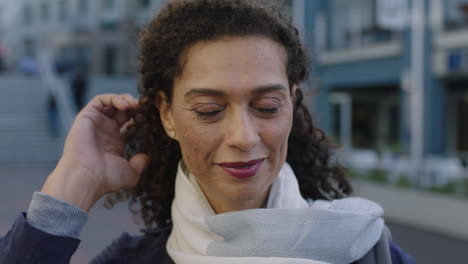 slow motion portrait of beautiful mixed race woman looking at camera smiling happy fixing hair wearing scarf in urban background