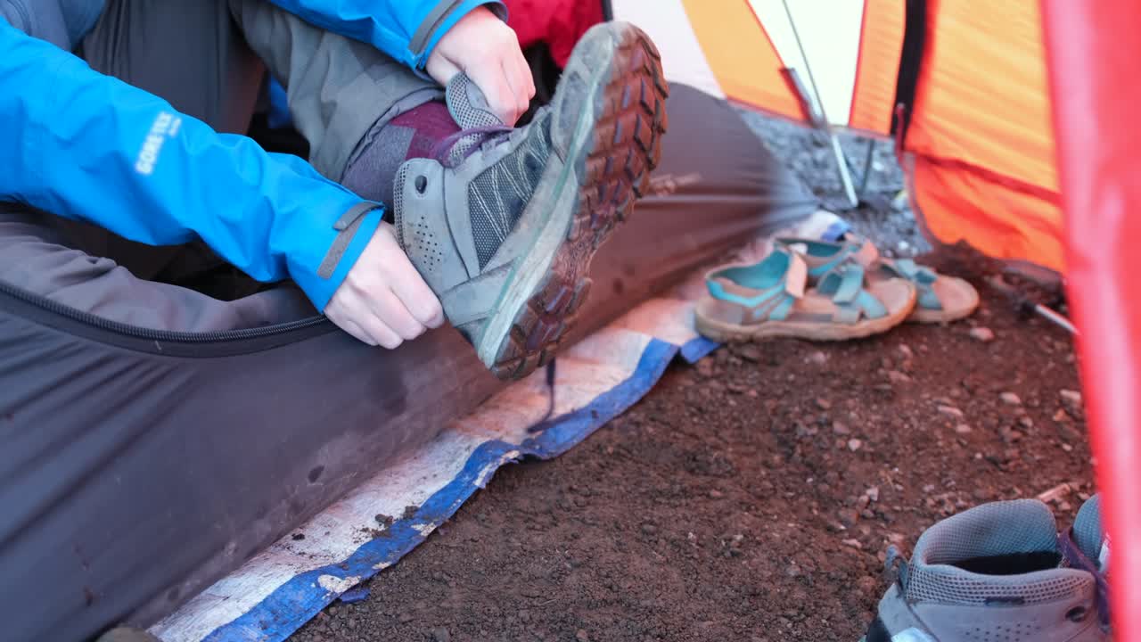 A girl in a tent sits and puts on trekking boots before climbing Mount Kilimanjaro.