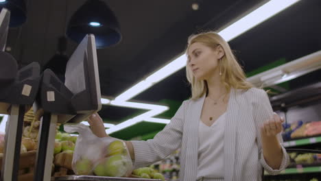 young woman weighing apples on the electronic scales. housewife shopping in a supermarket in the department of fruit and vegetables. slow motion. sale shopping consumerism and people concept