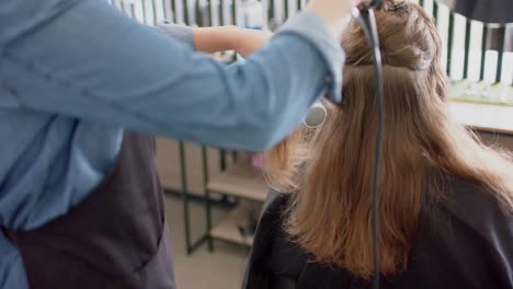 Caucasian-female-hairdresser-styling-client's-long-hair-with-brush-and-hairdryer,-in-slow-motion