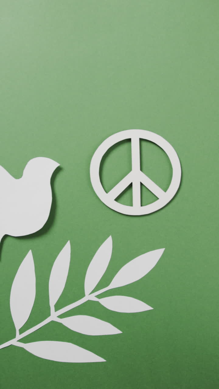 Vertical video of white dove with peace sign and leaf and copy space on green background