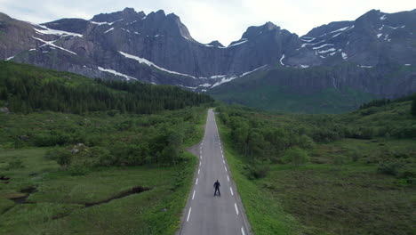 Ascending-drone-shot-of-a-man-skating-on-a-empty-road-in-Lofoten-Islands-during-midnight-sun-season