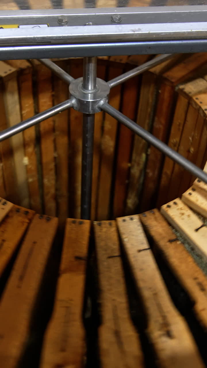 Electric metal barrel machine loaded with wooden frames. The equipment starts to rotate for getting fresh honey from honeycombs. Vertical video