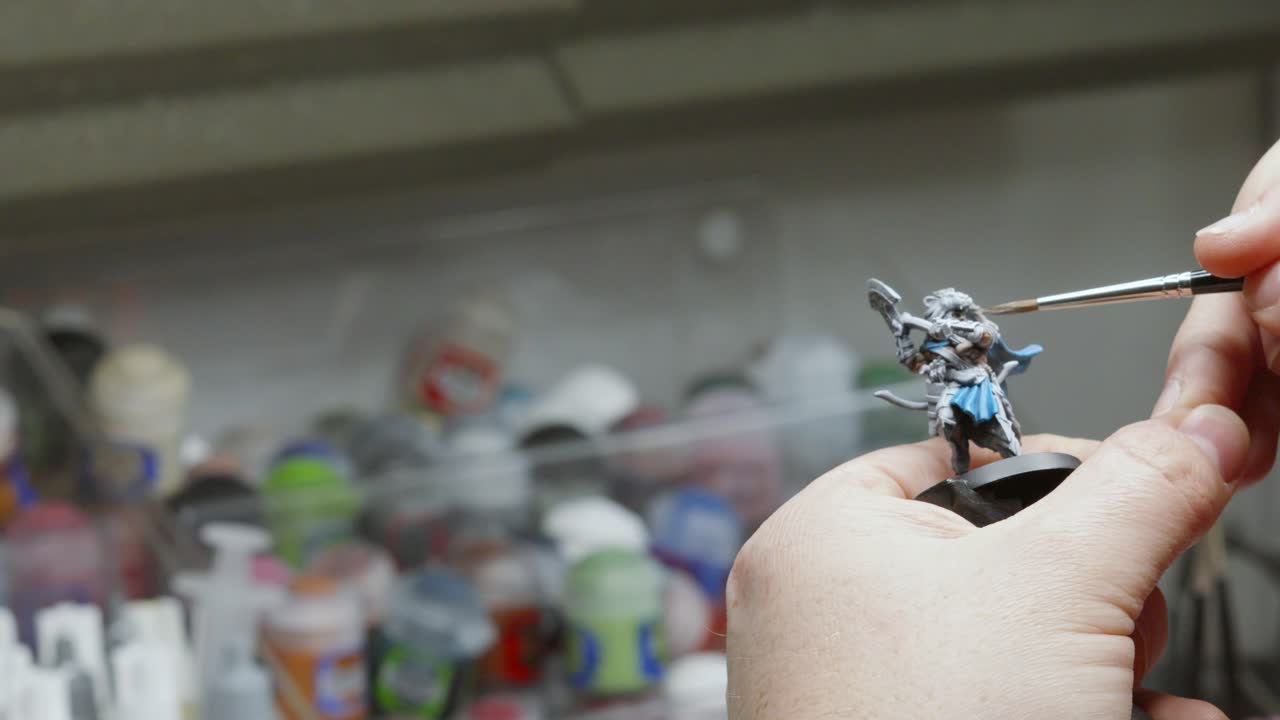 Art Studio Setting with Artist Painting Miniature Fantasy Figure Model with Paint Brush and Different Color Pots in Background 4K