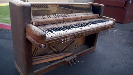 Old-Broken-Piano-Sitting-Alongside-Curb,-Trash,-Dumpster