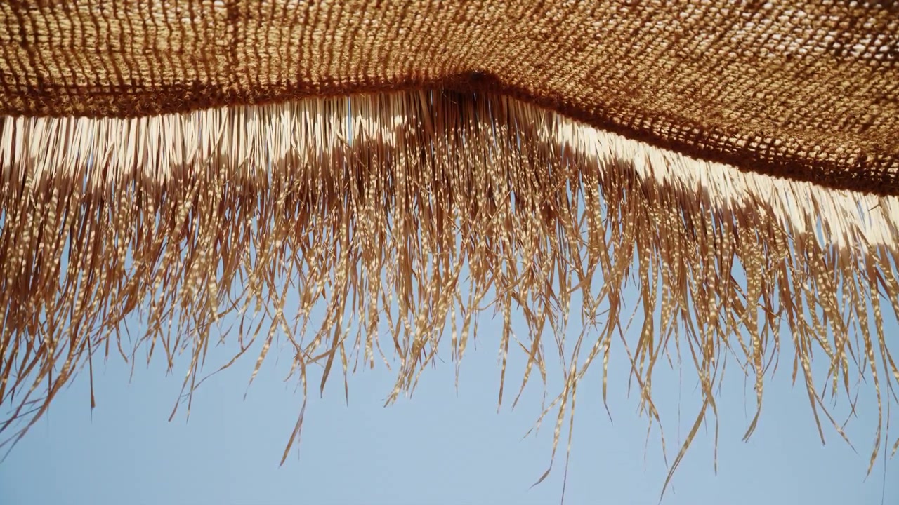 Primo piano dal basso di una tettoia in paglia intrecciata, illuminata dalla calda luce del sole.