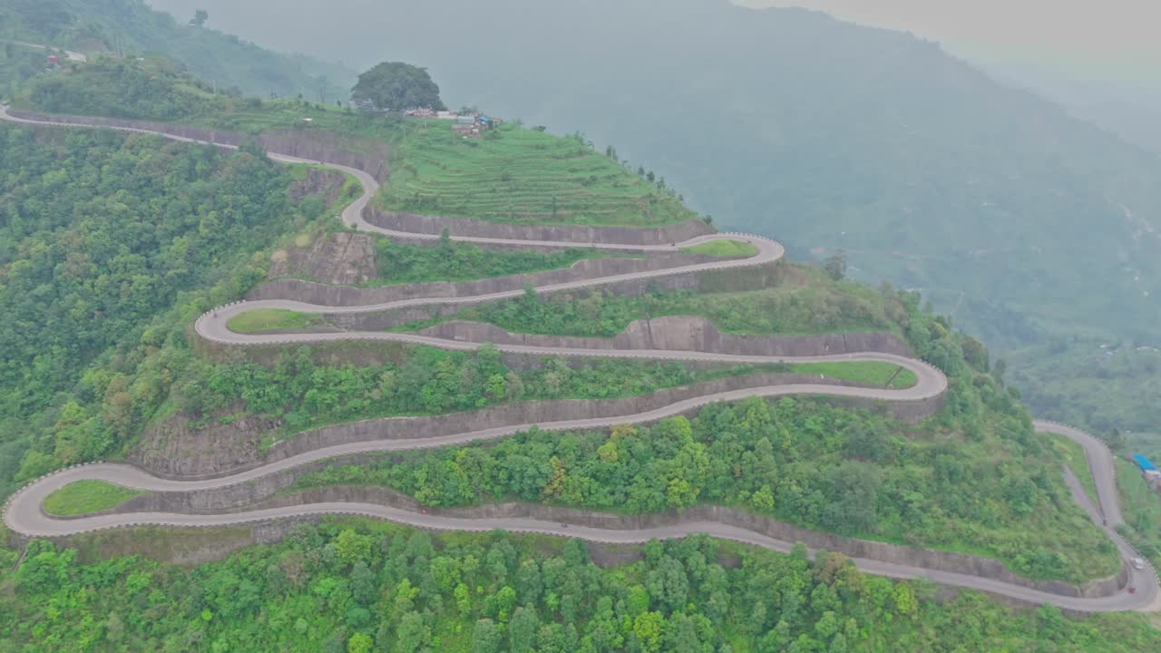 A serpentine road curves gracefully through vibrant green mountains, offering a breathtaking view of natural beauty and human engineering in harmony, captured from a high-altitude aerial perspective.