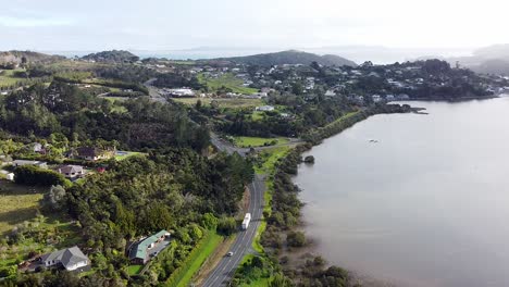 The-historic-town-of-Mangonui-in-Northland,-New-Zealand,-Aotearoa-with-traffic-arriving-and-leaving-aerial-drone