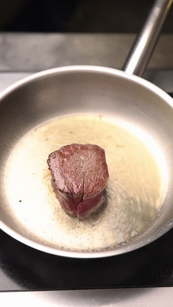 Primo piano di una bistecca che sfrigola e viene condita in una padella calda
