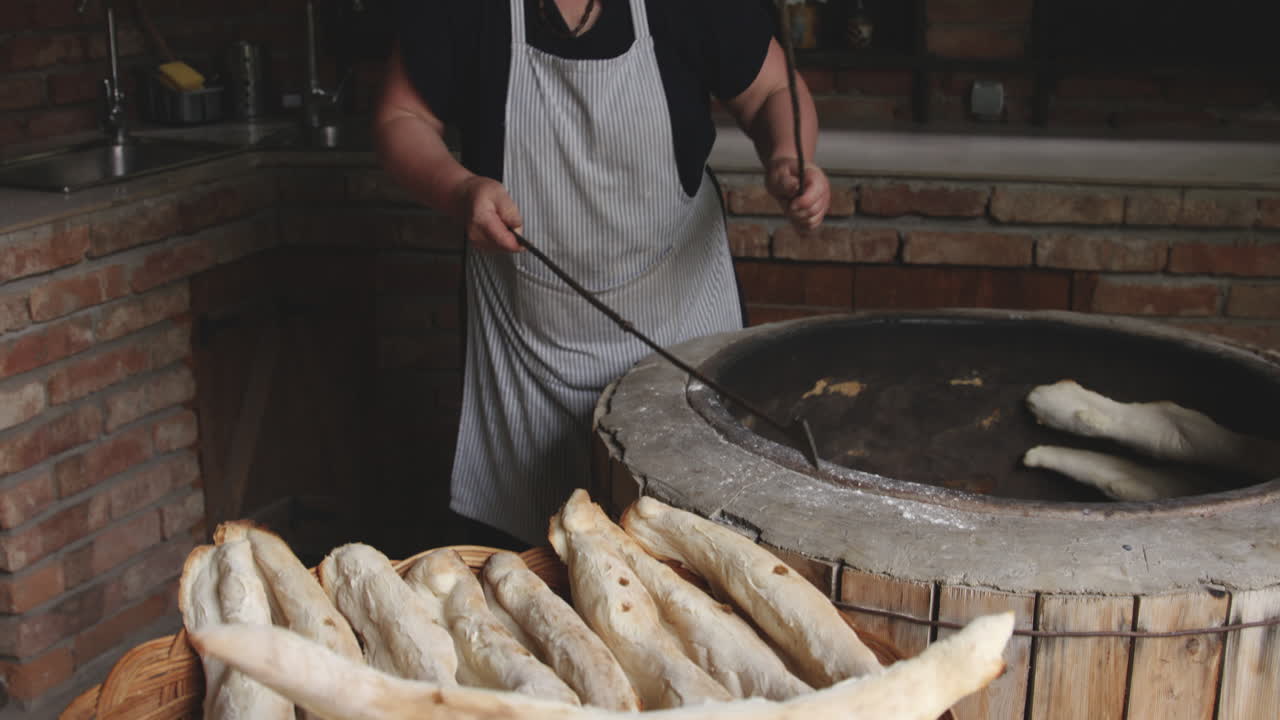 mujer panadera sacando el pan shoti horneado de un horno de arcilla redondo rústico usando un palo de hierro