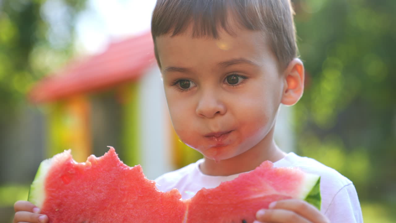Lovely Caucasian baby boy eating a slice of fresh juicy watermelon. Portrait of a kid enjoying summer fruit. Close up.