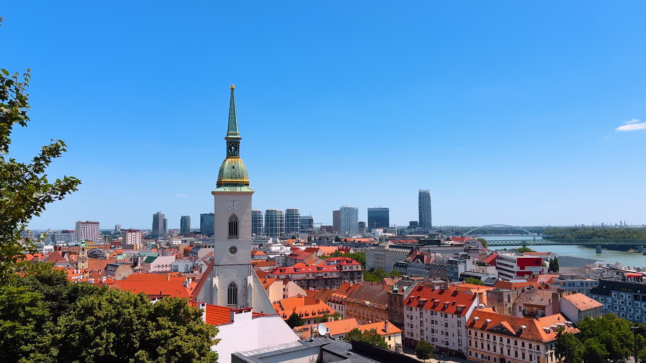 View over the orange roofs of old town in Bratislava, Slovakia. Tower of St. Martin's Cathedral with a clock. New modern buildings at backdrop