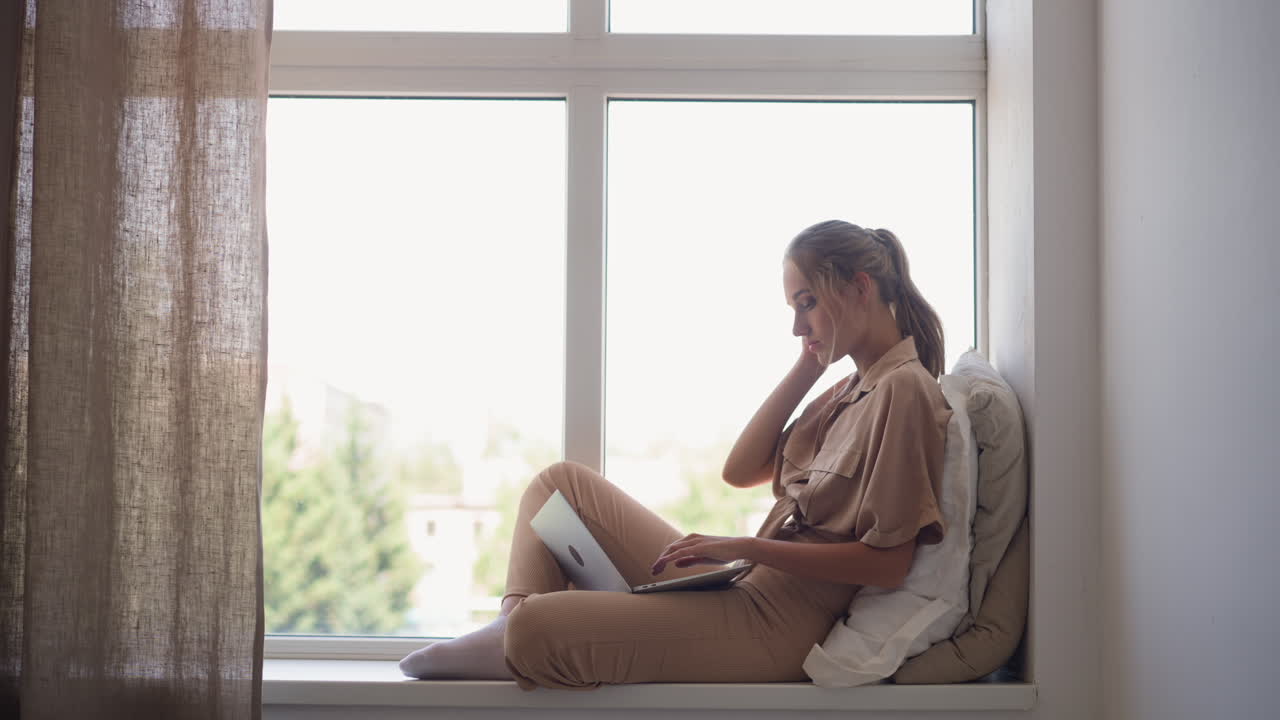 창 ⁇ 에 앉아서 노트북을 통해 일하는 프리랜서 여성