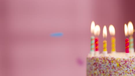 studio shot of paper confetti falling on birthday cake covered with decorations and candles being blown out 1