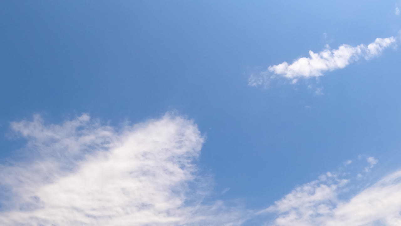 Blue summer sky with few light cirrus cloudscape floating by. Beautiful sunny day sky timelapse. Low angle view.