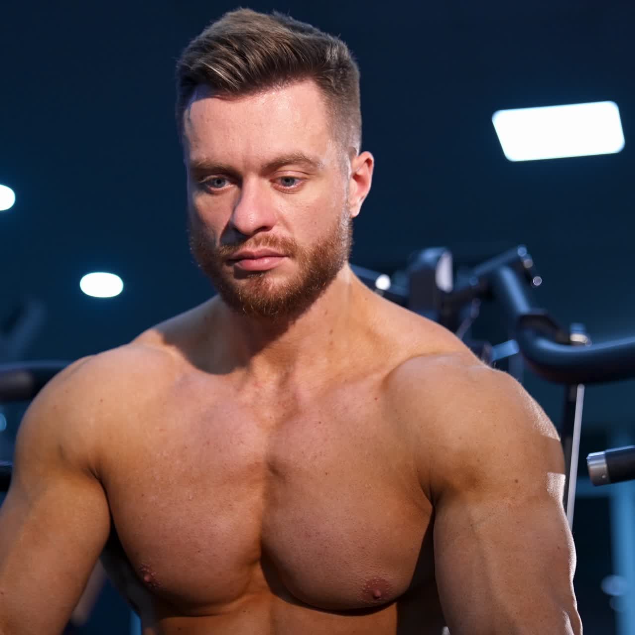 Handsome man with big muscles, posing at the camera in the gym. Modern sport equipment background. Serious bodybuilder