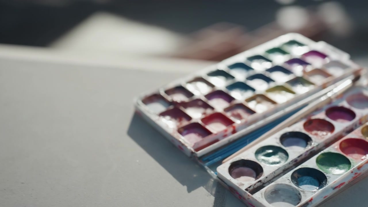 Primo piano ravvicinato di una bella tavolozza: donna bianca mescola acquerello su un cornicione sul tetto, colori vivaci e pennellate, sfumature con la punta delle dita e gocce di pittura, texture illuminate dal sole e scale di cemento sottostanti, concentrata e giocosa.