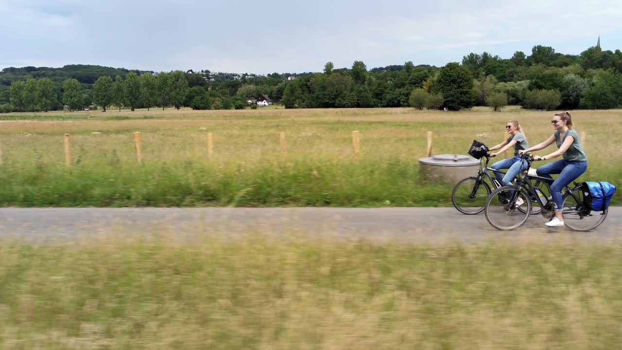 두 명의 젊은 여성이 을 가로질러 자전거를 타고 추적하는 드론 측면 시각
