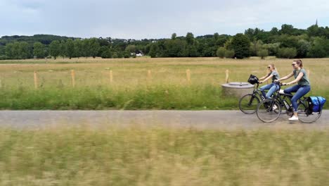 drone side view tracking two young women riding bikes through fields